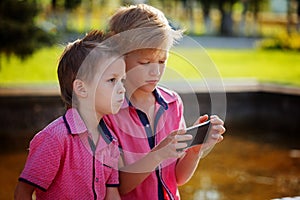 Two little boys playing games on mobile phone in sunny day.