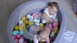 Two little boys playing in a pool of colored balls. Baby gets to his feet