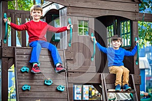 Two little boys playing together and having fun. Lifestyle family moment of siblings on playground. Kids friends play on tree