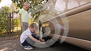 Two little boys are repairing a car, they lift the car with a jack.