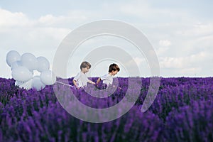 Two little boys run through lavender field with white balloons, sunny day,