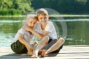 Two little boys sit in an embrace on the banks of the river. Concept of friendship and fraternity