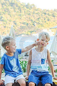 Two little boys are sitting on a bench near a beach laughing and engaging playfully