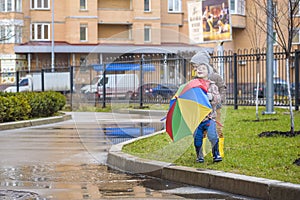 Two little boys, squat on a puddle, with little umbrellas