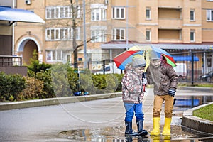 Two little boys, squat on a puddle, with little umbrellas