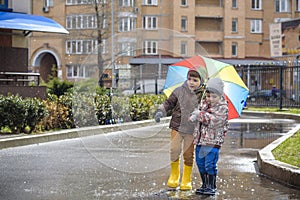 Two little boys, squat on a puddle, with little umbrellas