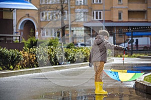 Two little boys, squat on a puddle, with little umbrellas