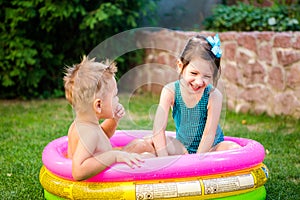 Two little brother and sister playing and splashing in pool on hot summer day. Children swimming in kid pool. Two cheerful cute