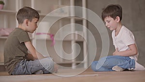 Two little brothers sitting on the floor playing with the toy car sitting on the floor at home. Siblings spending time