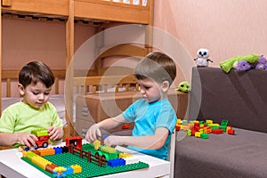 Two little caucasian friends playing with lots of colorful plastic blocks indoor. Active kid boys, siblings having fun building an