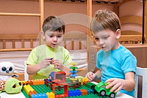 Two little caucasian friends playing with lots of colorful plastic blocks indoor. Active kid boys, siblings having fun building an