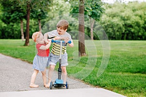 Two little Caucasian preschool children fighting in park outside. Boy and girl can not share one scooter.