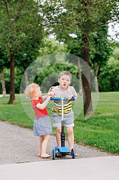 Two little Caucasian preschool children fighting in park outside. Boy and girl can not share one scooter.