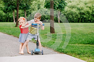 Two little Caucasian preschool children fighting in park outside. Boy and girl can not share one scooter.