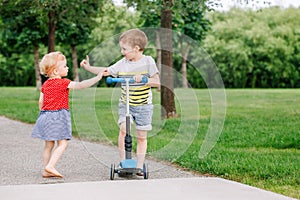 Two little Caucasian preschool children fighting in park outside. Boy and girl can not share one scooter.