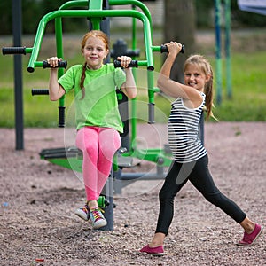 Two little cheerful girls is engaged in sport fitness equipment on the Playground.