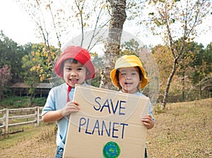 Two little child girl siblings holding`Save the planet` Poster showing a sign protesting against plastic pollution in the forest.