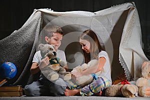 Two little child play at home in the evening to build a camping tent to read books with a flashlight and sleep inside