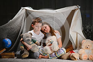 Two little child play at home in the evening to build a camping tent to read books with a flashlight and sleep inside. Concept of