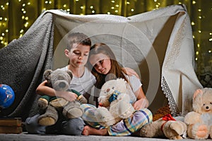 Two little child play at home in the evening to build a camping tent to read books with a flashlight and sleep inside. Concept of