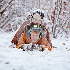 Two little children, boy brothers playing and lying in snow outdoors during snowfall. Active leisure with children in winter on co