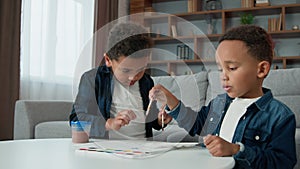 Two little children boys painting at home together. Ethnic brothers African American kids sibling paint picture with