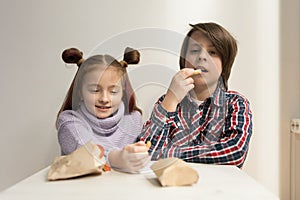 Two little children eating fries and sandwiches in a fast food restaurant for lunch. Cute girl with ponytails and handsome boy in