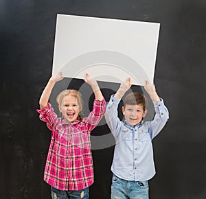 Two little children keeping blank paper sheet above their heads