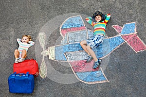 Two little children, kid boy and toddler girl having fun with with airplane picture drawing with colorful chalks on