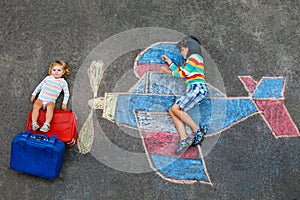 Two little children, kid boy and toddler girl having fun with with airplane picture drawing with colorful chalks on