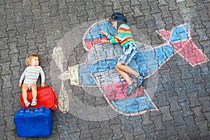 Two little children, kid boy and toddler girl having fun with with airplane picture drawing with colorful chalks on