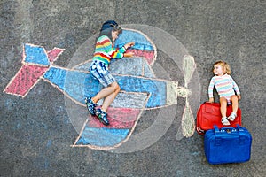 Two little children, kid boy and toddler girl having fun with with airplane picture drawing with colorful chalks on