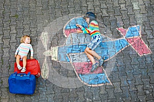 Two little children, kid boy and toddler girl having fun with with airplane picture drawing with colorful chalks on