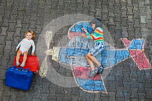 Two little children, kid boy and toddler girl having fun with with airplane picture drawing with colorful chalks on