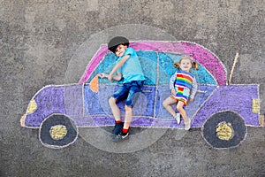 Two little children, kid boy and toddler girl having fun with with car picture drawing with colorful chalks on asphalt