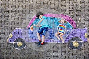 Two little children, kid boy and toddler girl having fun with with car picture drawing with colorful chalks on asphalt