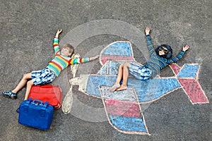 Two little children, kids boys having fun with with airplane picture drawing with colorful chalks on asphalt. Friends