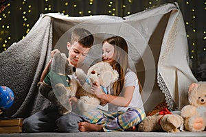 Two little children play at home in the evening to build a camping tent to read books with a flashlight and sleep inside