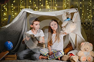 Two little children play at home in the evening to build a camping tent to read books with a flashlight and sleep inside. Concept