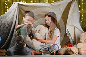 Two little children play at home in the evening to build a camping tent to read books with a flashlight and sleep inside. Concept