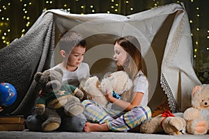 Two little children play at home in the evening to build a camping tent to read books with a flashlight and sleep inside. Concept