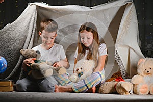 Two little children play at home in the evening to build a camping tent to read books with a flashlight and sleep inside. Concept