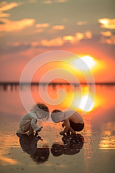Two little children playing on the beach during sunset. Reflection in water