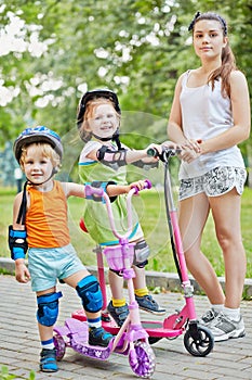 Two little children on scootes and teenage girl in