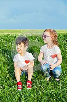 Two little children sit on edge of grassy slope,