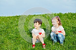 Two little children sit on edge of grassy slope, photo