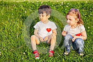 Two little children sit on grassy slope, red photo