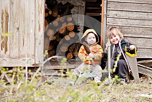 Two little children sit near a shed