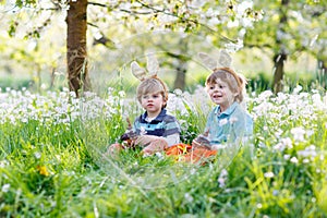 Two little children wearing Easter bunny ears and eating chocolate