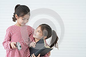 Two little cute children girls, playing hugging while reading a book with magnifying glass while standing on white background.